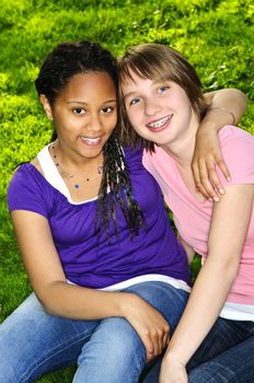 Two teenage girls sitting on grass and hugging