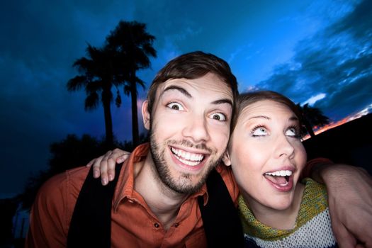 Young couple making funny faces against a blue and red sunset