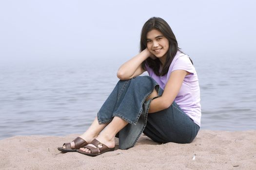 Young girl sitting on beach by lake on misty foggy day