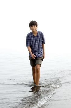 Young teen boy wading along shoreline of beach