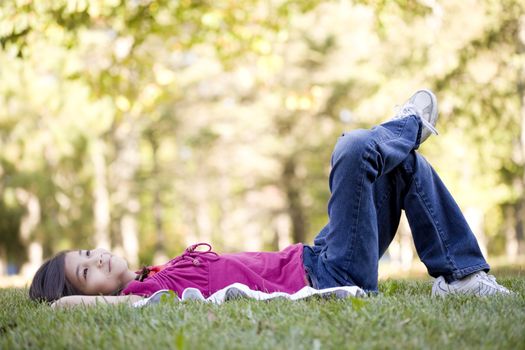 Little girl lying on grass lawn thinking, one leg crossed over the other