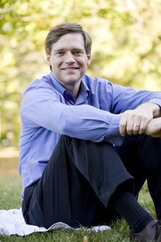 Handsome businessman sitting on lawn, arms wrapped around knees