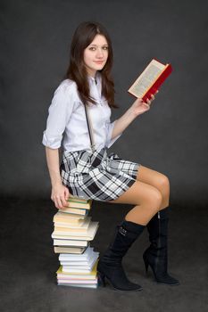 The beautiful young woman reads sitting on a pile of books on a black background
