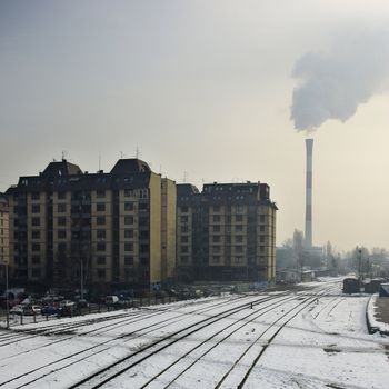 Urban winter landscape with train tracks and smoking chimney.