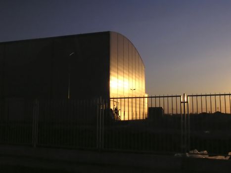 Industrial building at sunset with sun reflection and against clear blue sky.