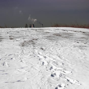Winter urban landscape, footsteps in snow, industrial chimney in background.