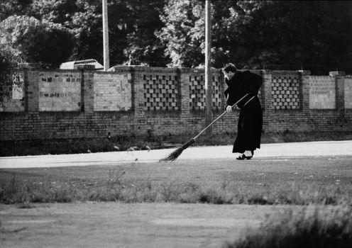 Black and white picture of a monk cleaning a yard with swab.