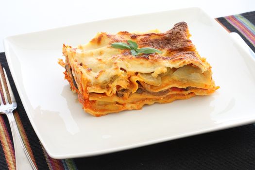 Vegetarian lasagna with eggplant, courgette, sweet potatoes and tomato sauce on a white plate.
