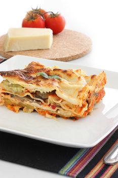 Vegetarian lasagna with eggplant, courgette, sweet potatoes and tomato sauce on a white plate.