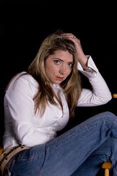 Attractive woman in white blouse and jeans, reclining in chair and isolated over black