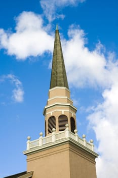 Close up of a small town church steeple against a blue sky with clouds