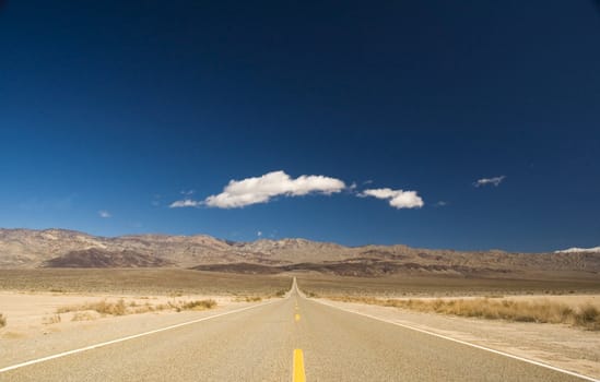 Straight road in Death valley heading into the mountains with wispy clouds overhead