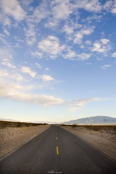 Straight road in Death valley heading into the mountains with wispy clouds overhead