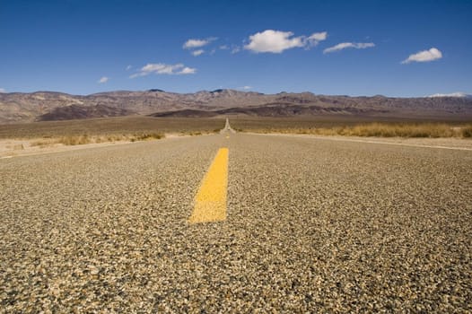 Straight road in Death valley heading into the mountains with wispy clouds overhead