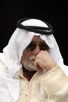 Arabic looking gentleman in a dishdash, traditional headress and wearing sunglasses, making getures during conversation