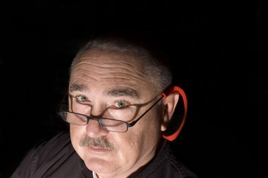 Mustached Man wearing glasses in the dark with direct light looking up