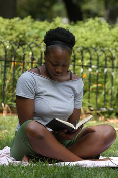 Young african american woman sits and reads in the park