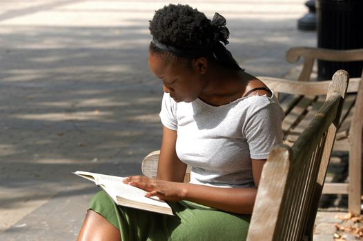Young african american woman reads on a park bench.