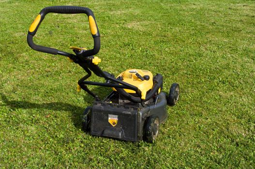 Yellow lawn mower on the green field.