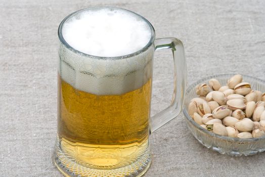 Mug with beer and dish with pistachios on a table-cloth.