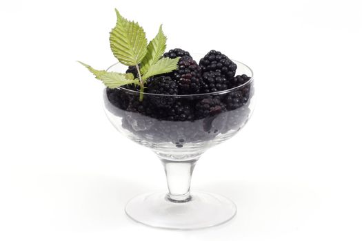 Fresh blackberries with leaves in a glass over white background