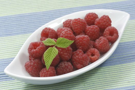 Fresh raspberries with raspberry-leaves in a white bowl