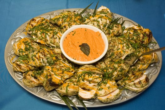 Grilled chicken dish with sauce and dressing on a silver plate over a blue tablecloth