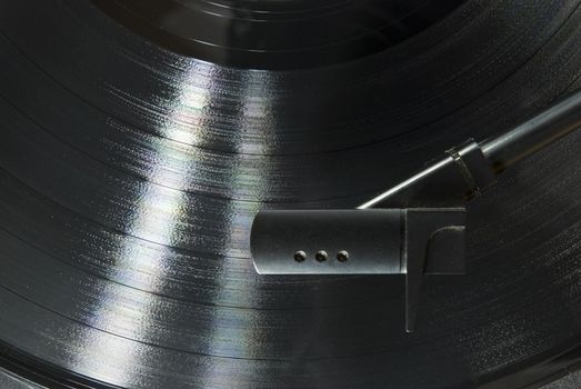 Cropped image shot directly from above of a record player needle, with LP underneath