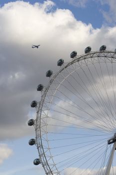 The famous London Eye. Once the largest ferris wheel in the world, still a popular tourist attraction and a landmark in London's skyline. Other angle, with airplane in the background. 