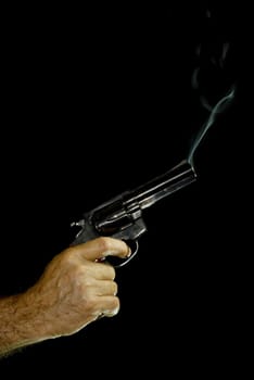 Male hand holding a .38 caliber revolver, with bluish smoke coming out of it. Black Background.