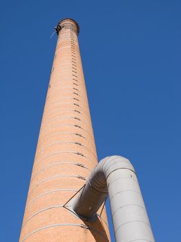 Huge industrial chimney with unrecognizable workers hanging from it. Blue sky.