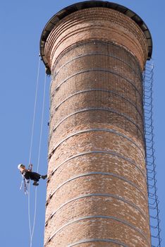 Cropped shot of an unrecognizable workers hanging from a high industrial brick chimney. Blue sky in the background.