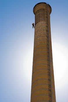 Huge Industrial Chimney with unrecognizable workers hanging from it. Blue sky.