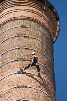 Cropped shot of an unrecognizable workers hanging from a high industrial brick chimney. Blue sky in the background.
