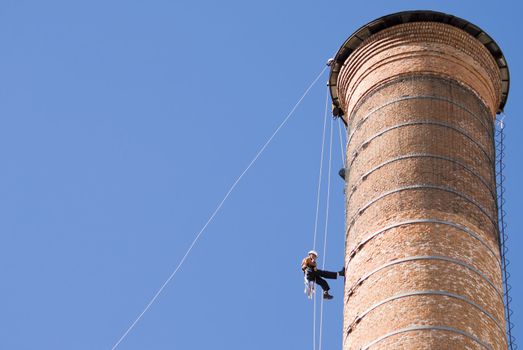 Cropped shot of an unrecognizable workers hanging from a high industrial brick chimney. Blue sky in the background, with huge copy space.