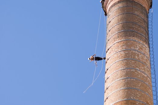 Cropped shot of an unrecognizable workers hanging from a high industrial brick chimney. Blue sky in the background, with huge copy space.