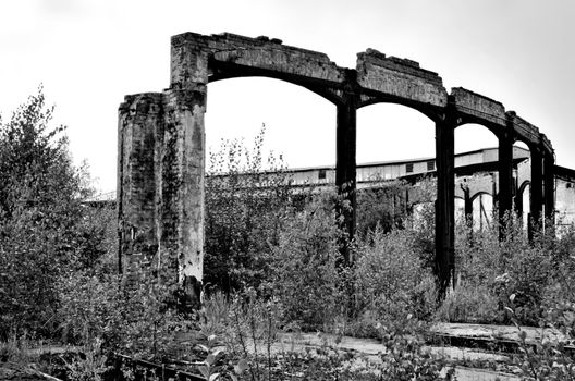 Rotting ruin of an industrial building, the remains of a huge round locomotive shed, which was destroyed by a fire. Totally abandoned area, plants growing everywhere.