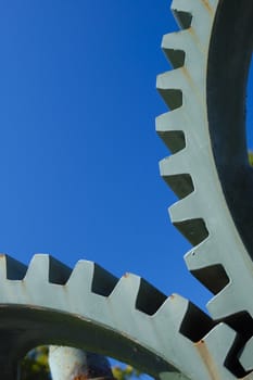 Two old interlocking gear wheels,  slightly rust-streaked, from some unidentifiable piece of machinery, set against a clear blue sky. Space for text.