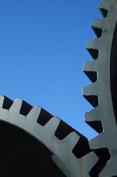 Two old interlocking gear wheels,  slightly rust-streaked, from an abandoned piece of machinery, set against a clear blue sky. Space for text.