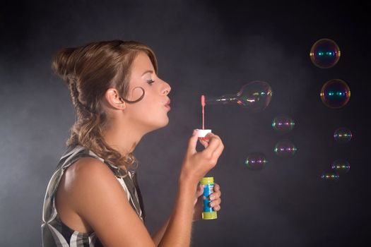 Pretty blond girl blowing bubbles on black background