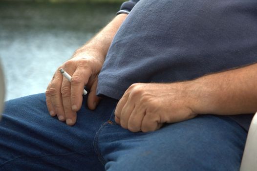 Image of a hand holding a burning cigarette between the fingers.