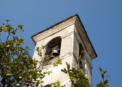 The top of a bell tower in the blue sky, with tree branches