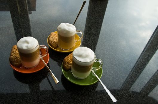 Black granite kitchen dresser with three glass mugs "cafe au lait", colorful saucers, cookies and reflection of the sky through window