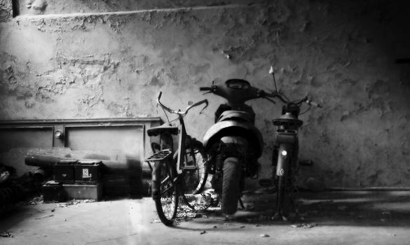 Two bikes and a scooter in an old garage, black and white