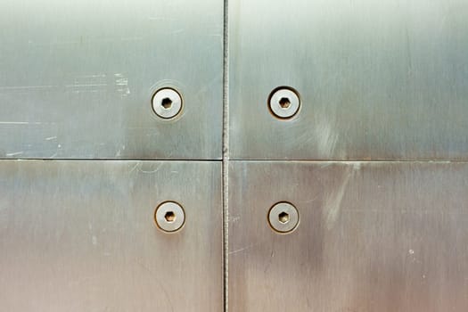 Stainless steel screws holding brushed steel panel on wall of modern building.