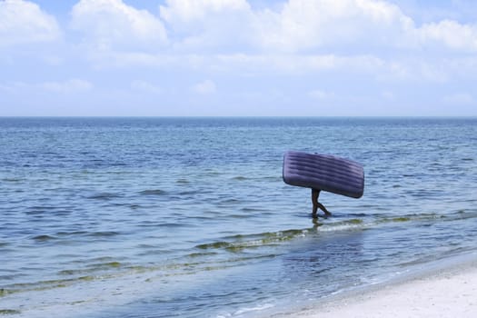 The man carries an inflatable mattress in the sea