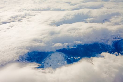 Above the clouds looking down between them on snowy mountain landscape.