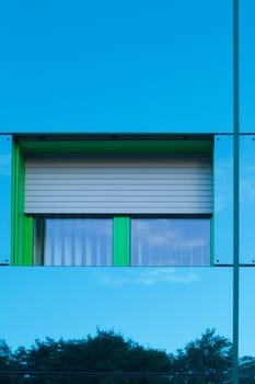 Mirrored image of environment of office building on highly reflective exterior wall with window.