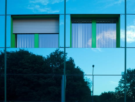 Mirrored image of environment of office building on highly reflective exterior wall with two windows.