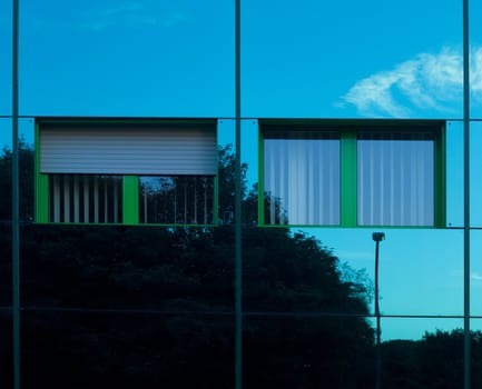 Mirrored image of environment of office building on highly reflective exterior wall with two windows.